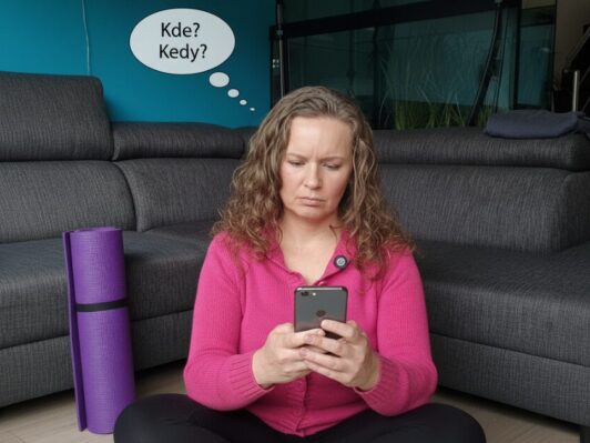 Žena sedí na zemi s mobilom a hľadá informácie o joge, no nevie kde a kedy sa cvičí